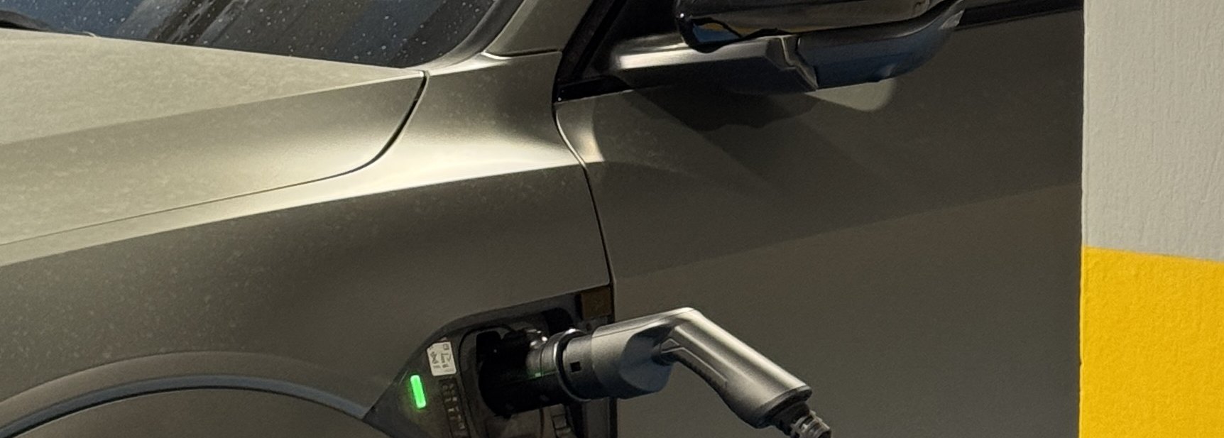An electric car charging at a wall charger in a car park